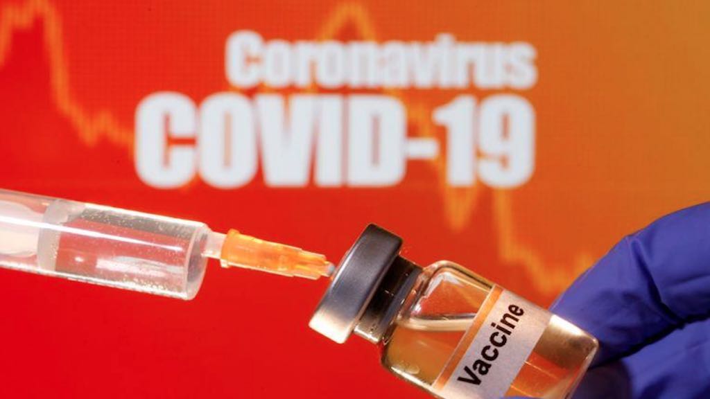 Foto de ilustração mostra frasco com rótulo de vacina em frente a cartaz de covid-19