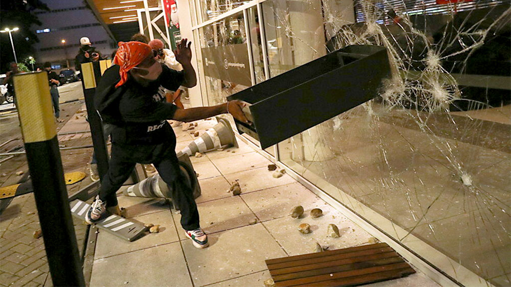 Manifestante quebra uma das vidraças do supermercado Carrefour, em São Paulo, durante protesto pela morte de um homem negro