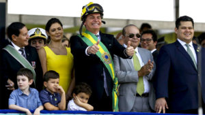 Trajado com a faixa presidencial, capacete e óculos de segurança, Bolsonaro acena aos adeptos, na Esplanada dos Ministérios