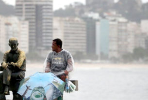 Vendedor ambulante aposta na venda de guarda-chuvas para os próximos dias, em Copacabana, onde descansa ao lado da estátua do poeta Carlos Drummond de Andrade