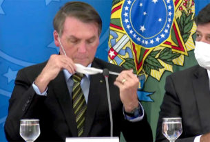 Bolsonaro se atrapalha na hora de vestir a máscara higiênica, ao lado do ministro da Saúde, Luiz Henrique Mandetta