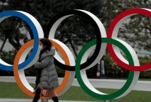 Pedestre caminha em frente a anéis olímpicos em Tóquio