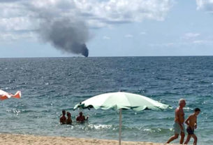 A fumaça do incêndio no barco de imigrantes pode ser vista da praia, em Crotone, na Cicília