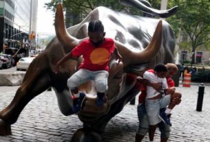 Crianças brincam em cima e estátua e touro localizada em frente à Bolsa de Valores de Nova York